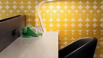 A room with a white desk, a green rotary phone, and a modern lamp.