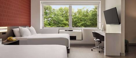 A hotel room with two beds, a desk, a chair, a TV, and a window with a view of trees.