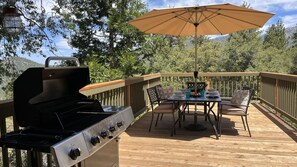 Una terraza al aire libre con una parrilla, una mesa con sillas y una sombrilla.