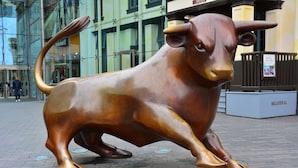Escultura de bronce de un toro en una zona pavimentada, con un edificio al fondo.