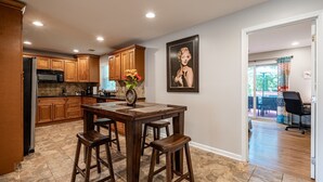 A kitchen with wooden cabinets, a dining table with stools, a microwave, and a vase with flowers. - Discover Your Beautiful Dream Vacation Rental at The Battery - Truist Park!  (Smyrna)