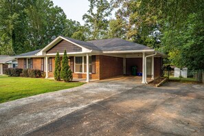 A two-story brick house with a covered front porch, a well-maintained lawn, and a driveway. - Discover Your Beautiful Dream Vacation Rental at The Battery - Truist Park!  (Smyrna)