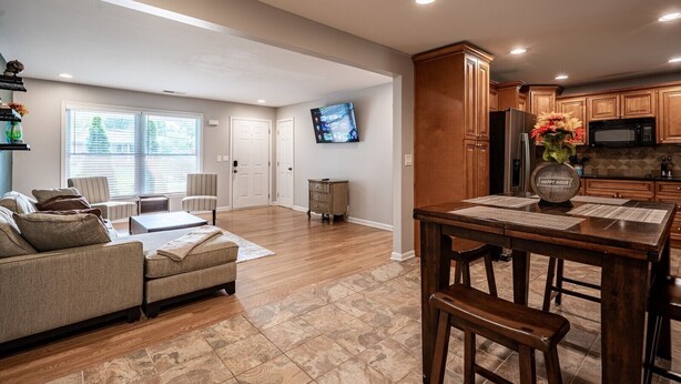 A spacious living room with a sofa, coffee table, and TV. There is a dining area with a wooden table and chairs. The kitchen has wooden cabinets and a microwave. - Discover Your Beautiful Dream Vacation Rental at The Battery - Truist Park!  (Smyrna)