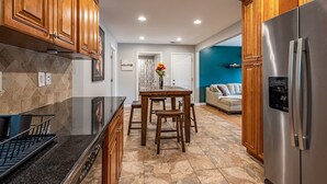 A modern kitchen with wooden cabinets, a stainless steel refrigerator, a granite countertop, and a dining area with a table and chairs. - Discover Your Beautiful Dream Vacation Rental at The Battery - Truist Park!  (Smyrna)