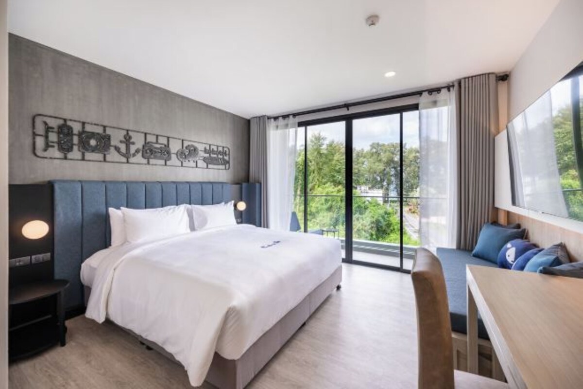 Una habitación de hotel moderna con una cama grande, un escritorio y un balcón con vistas a zonas verdes.