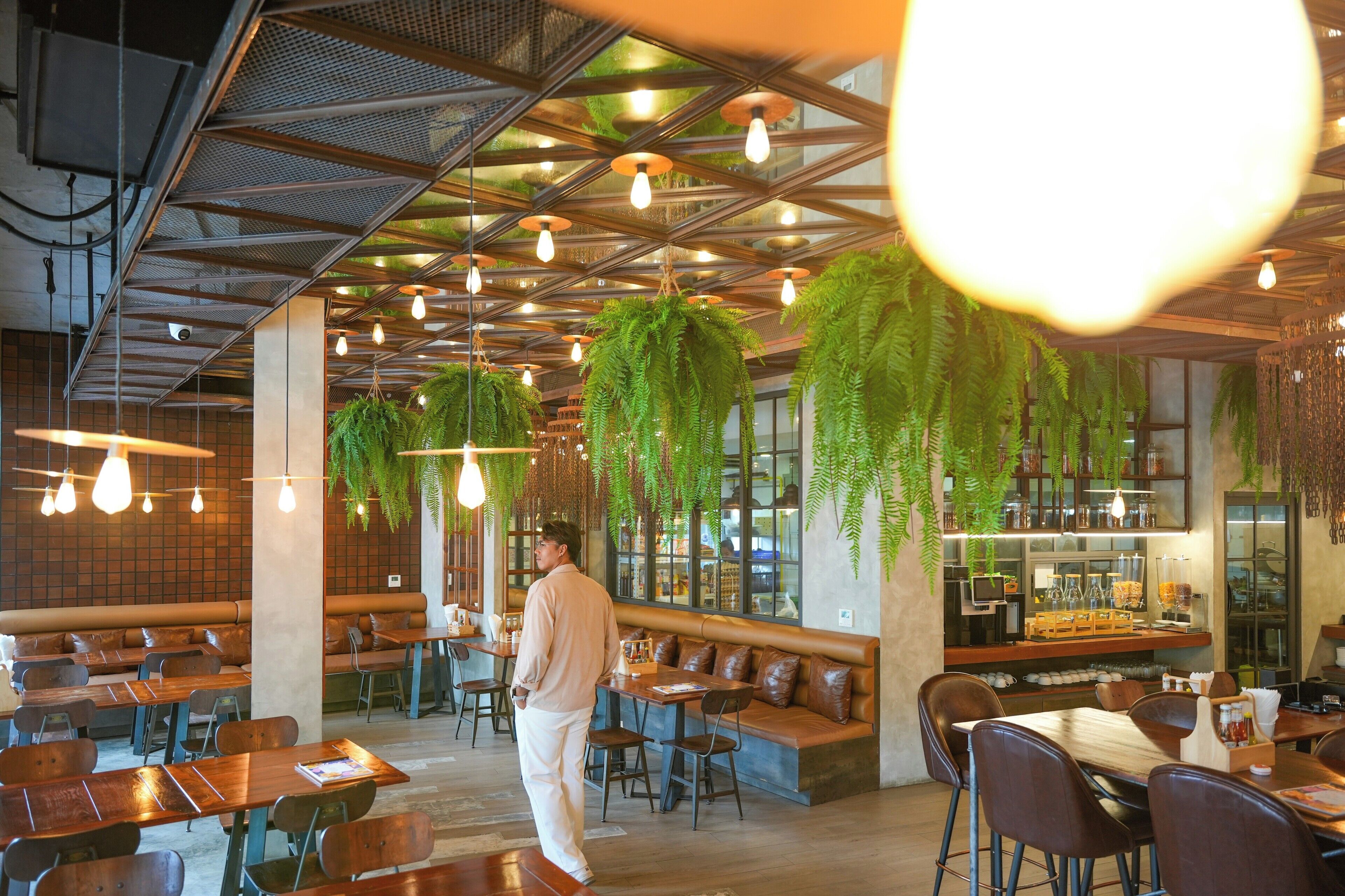 Un restaurant amb sostres alts, plantes penjants i diverses opcions de seients, incloent cabines i taules.