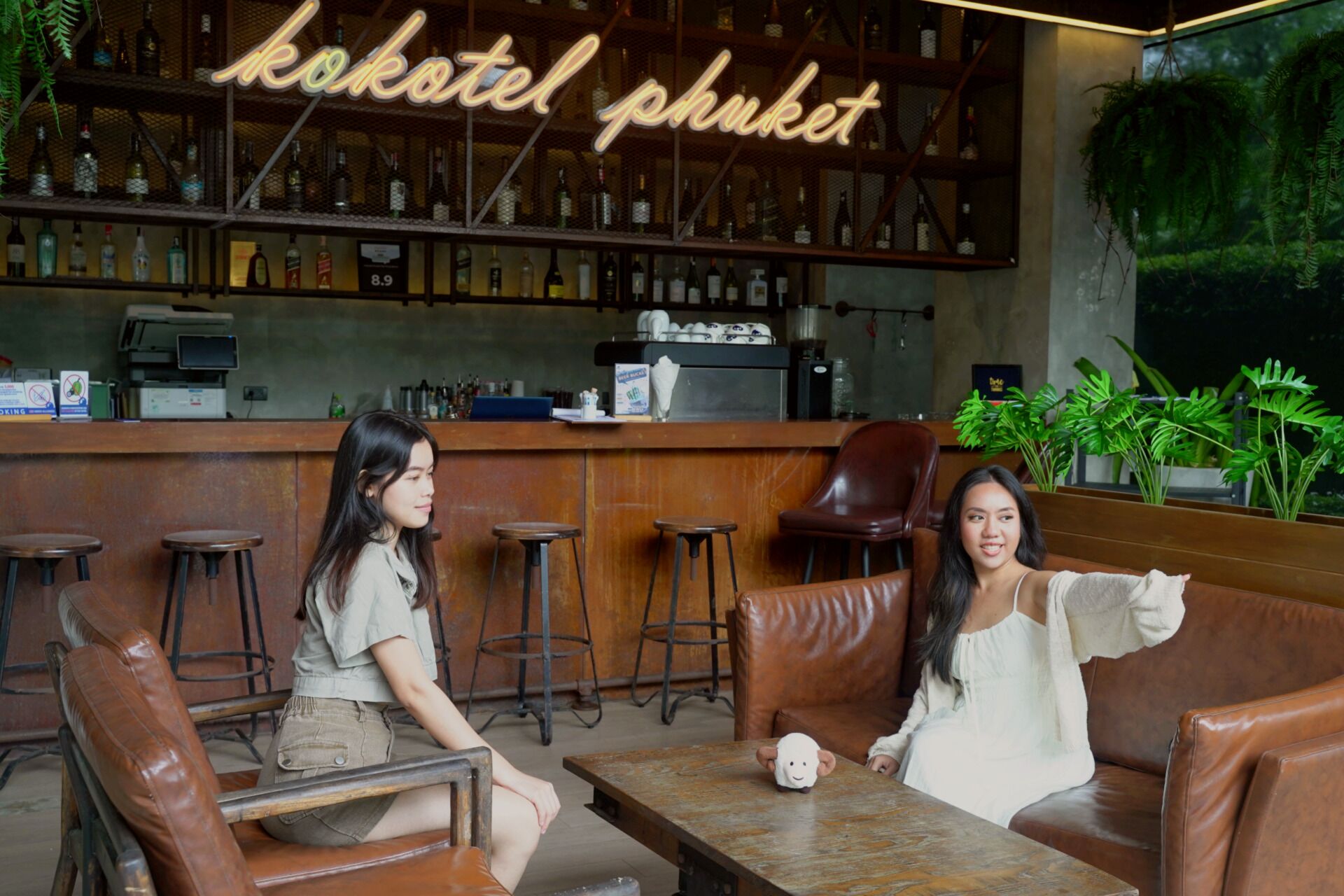 A bar area with a neon sign reading "bakotel phuket," leather seating, and a counter with various bottles.