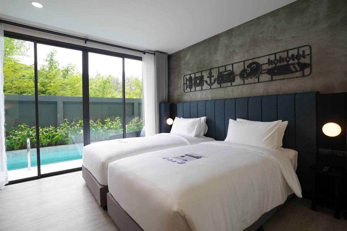 A hotel room with two beds, a large window with a view of greenery, and a wall decoration.