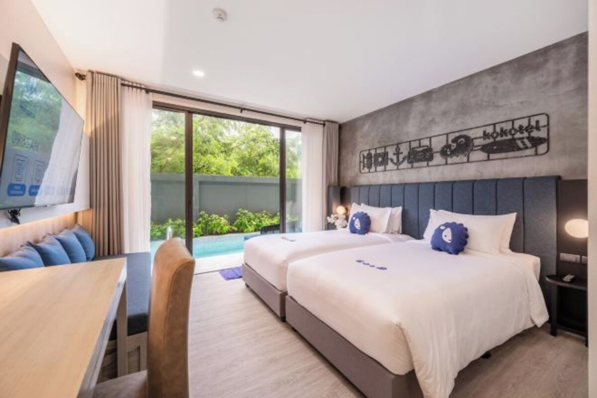 A hotel room with two beds, a dining area, and a large window with a view of greenery.