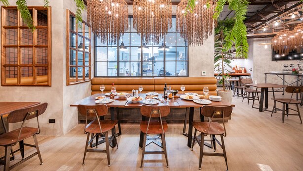 Un comedor con una larga mesa de madera preparada para una comida, rodeada de sillas y un amplio ventanal con vistas a la ciudad.