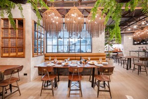 A dining area with a long wooden table set for a meal, surrounded by chairs, and a large window with a view of the city. - Kokotel Phuket Nai Yang Beach (Sa Khu)