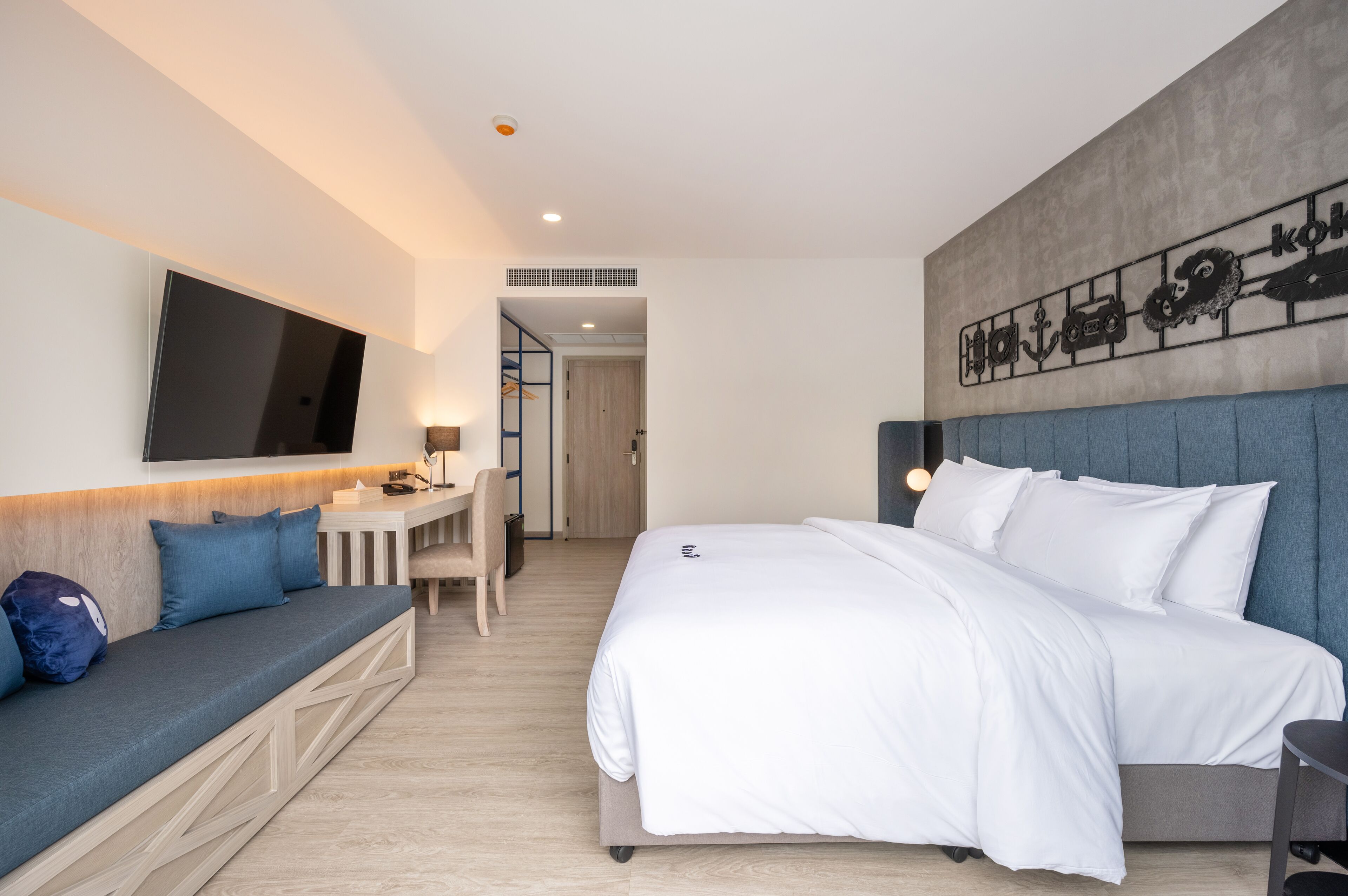 Una habitación de hotel moderna con una cama grande, un sofá, un escritorio y un televisor montado en la pared.