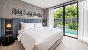 Una habitació d'hotel moderna amb un llit gran, un panell de capçal amb una làmpada, una taula auxiliar petita i vistes a vegetació a través d'una porta corredissa de vidre.