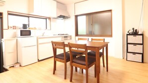 A compact kitchen with a dining table and chairs, a microwave, a refrigerator, and a window with blinds.