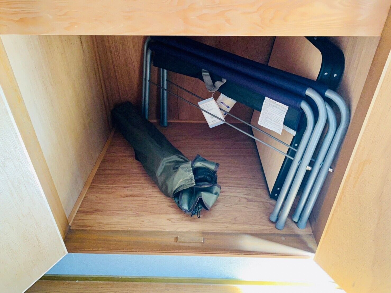 A compact storage space with a wooden floor, a metal rack, and a rolled-up item.