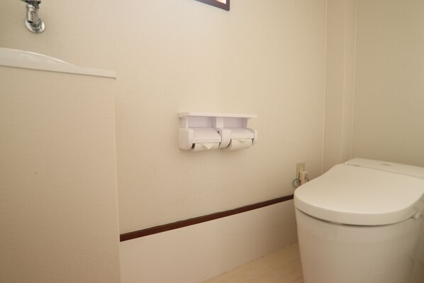 Un baño con un inodoro, un dispensador de papel higiénico fijado a la pared y un zócalo de madera.
