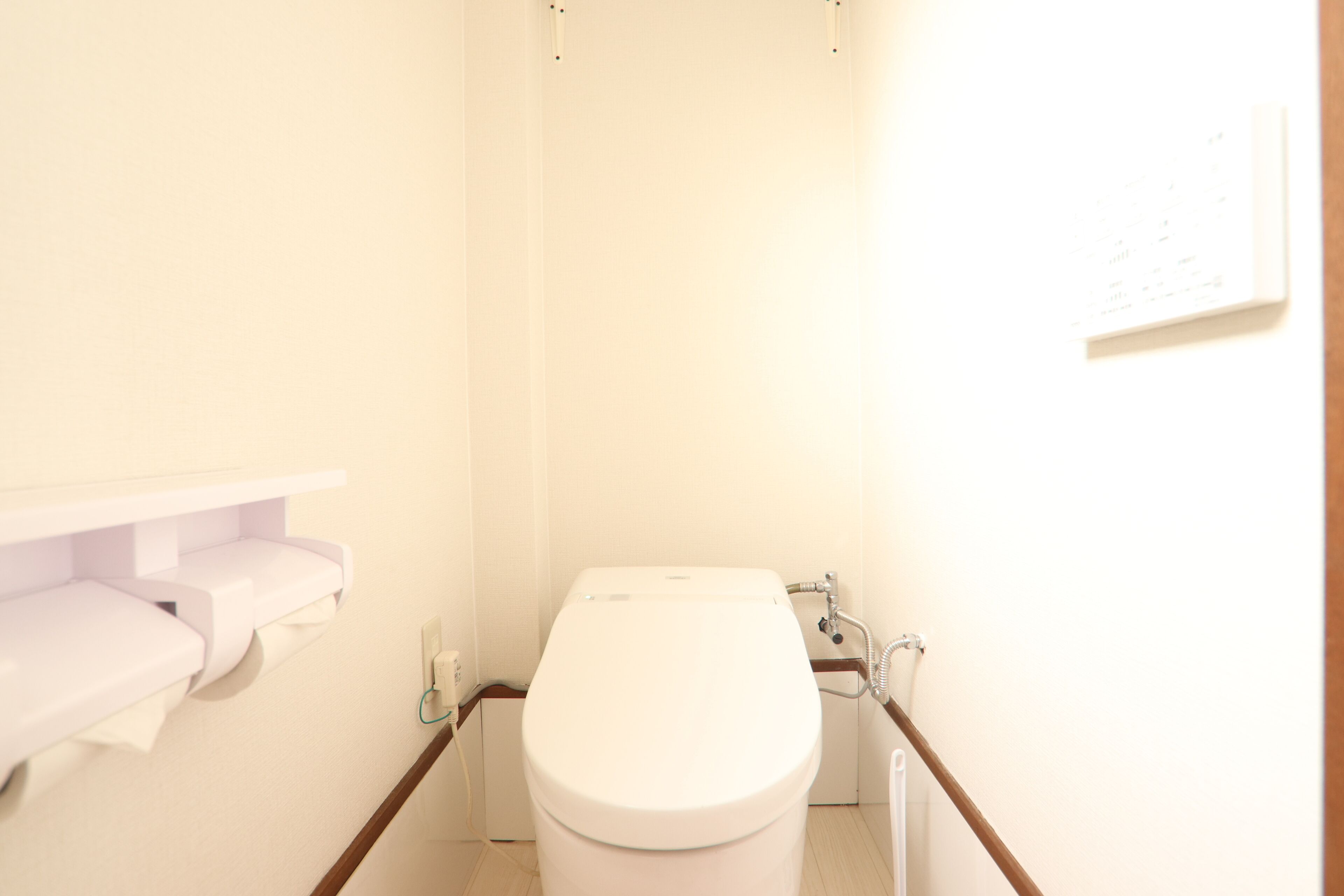 A small, narrow bathroom with a toilet, a toilet paper holder, and a wall-mounted light fixture.