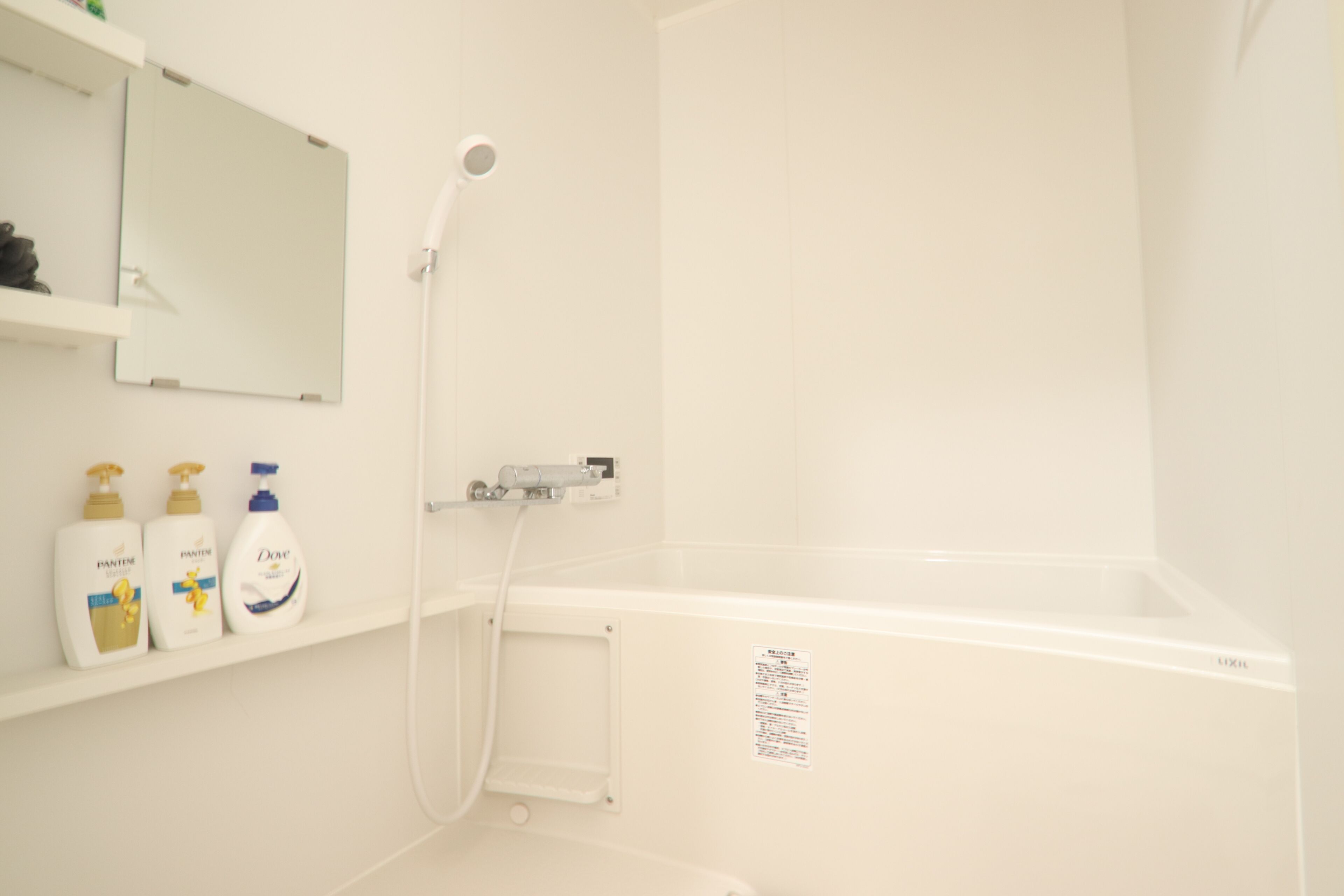 A bathroom with a white bathtub, a showerhead, and a shelf with three bottles of Dove body wash.
