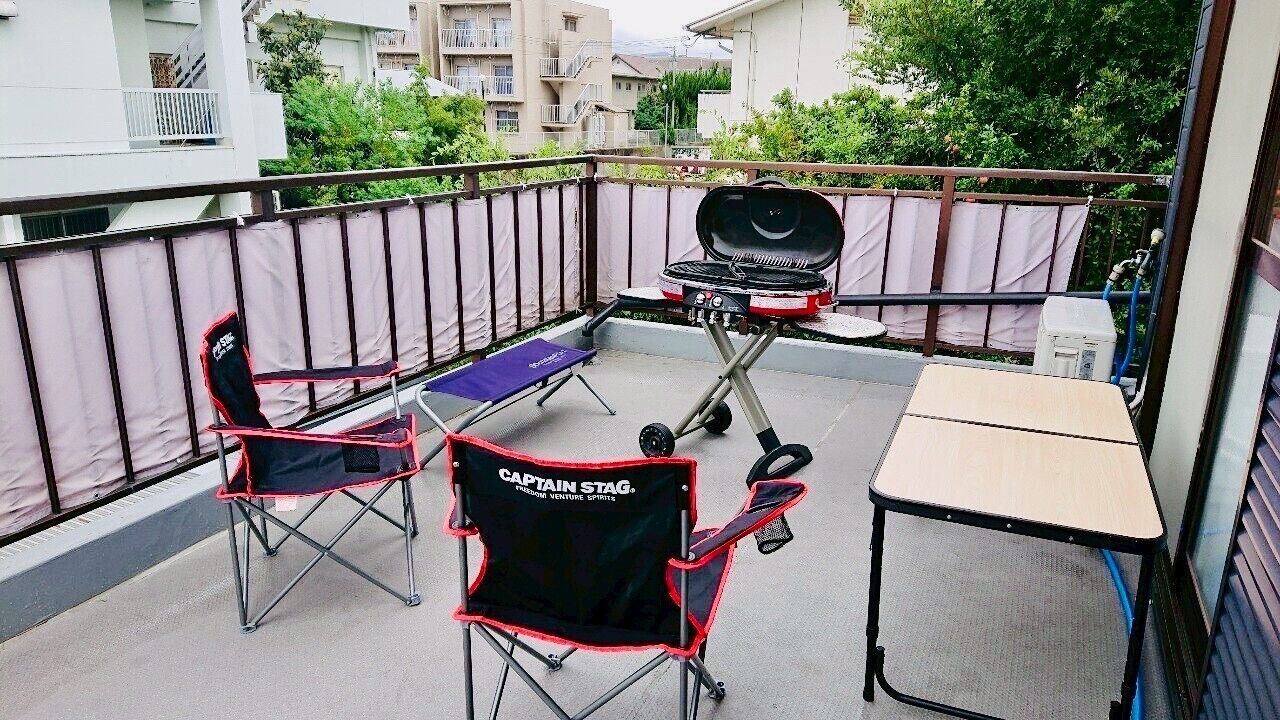 Varanda com churrasqueira, duas cadeiras dobráveis e uma mesa pequena.
