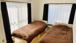 A small, clean room with two single beds, a bedside table, and a window with curtains.