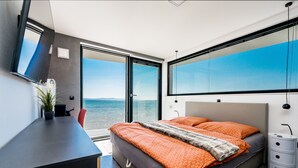 A modern bedroom with a large bed, a desk, and a view of the sea. - Jimmys Beach Privlaka: Penthouse dream, right by the sea and heated pool (Privlaka)