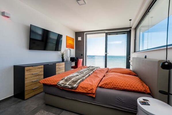 A modern bedroom with a bed, a desk, a TV, and a large window with a view.