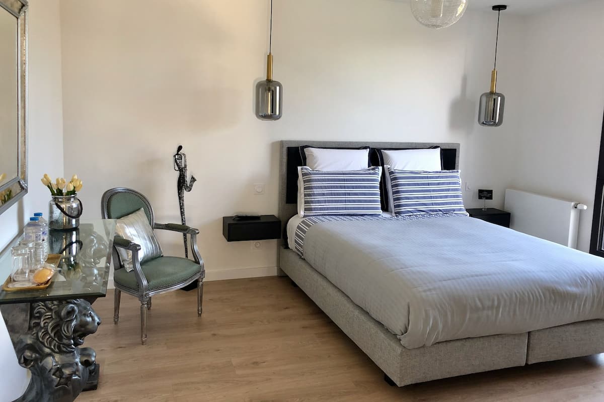 A bedroom with a bed, a chair, a table with a vase of flowers, and two pendant lights.