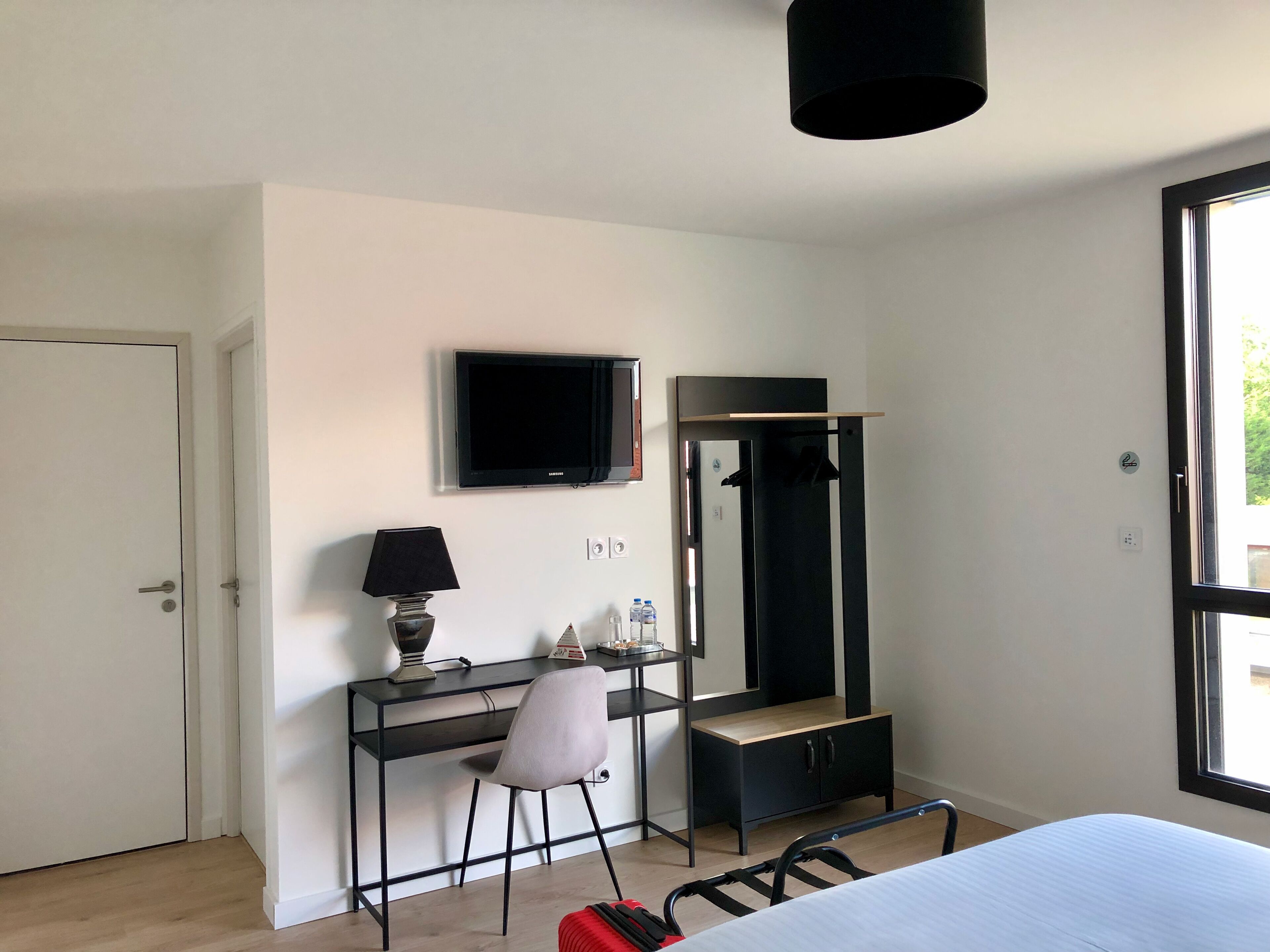 Une chambre à coucher avec un lit, un bureau et une chaise, une télévision, une armoire et une fenêtre.
