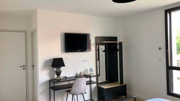 Une chambre à coucher avec un lit, un bureau et une chaise, une télévision, une armoire et une fenêtre.