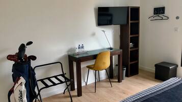 A hotel room with a bed, a desk with a chair, a TV, a coat rack, and a golf bag.