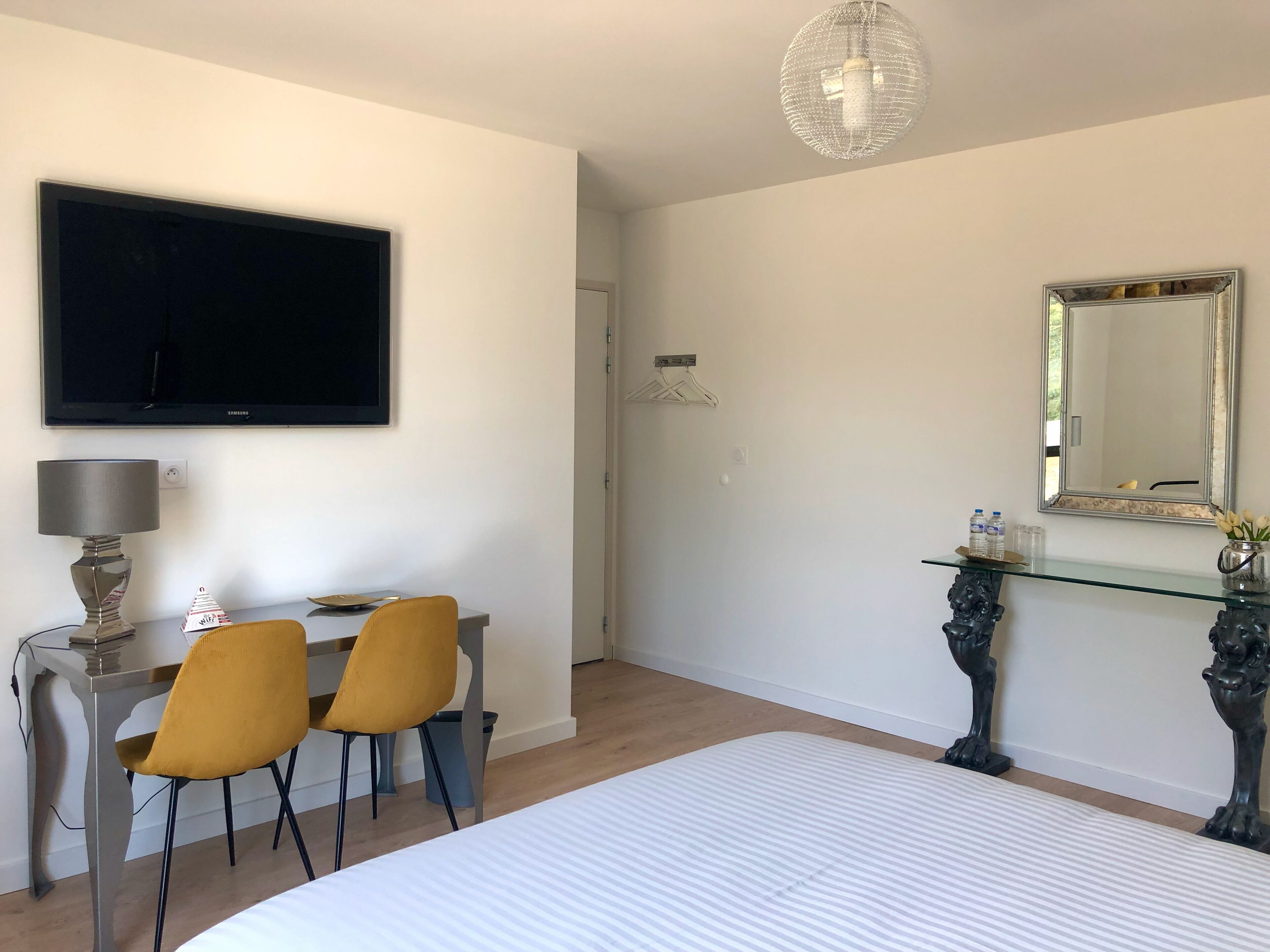 Una camera da letto con un letto, una scrivania con due sedie, una televisione, una lampada, uno specchio e una lampada a sospensione.