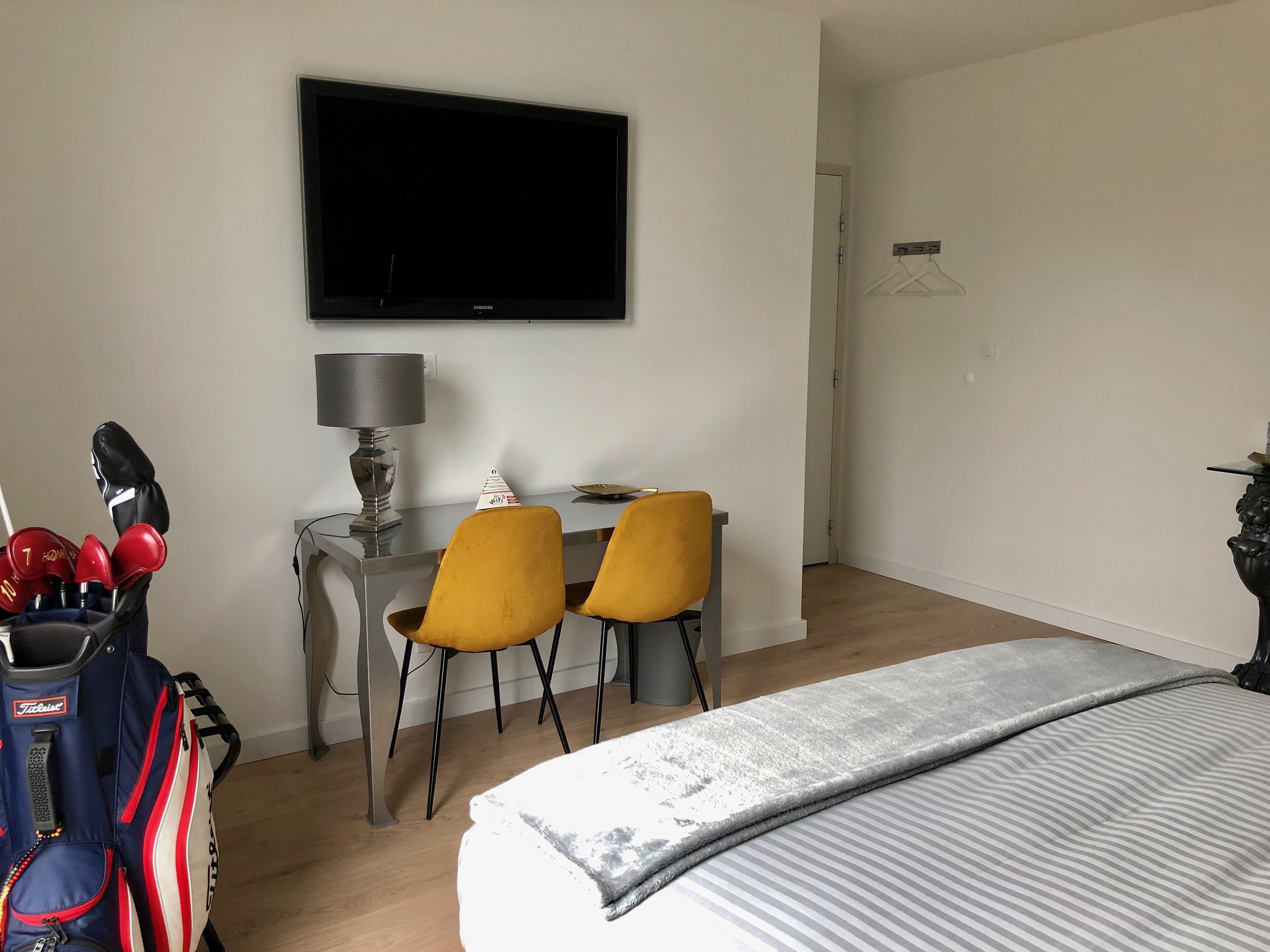 A hotel room with a bed, a desk with two chairs, a TV, and a bag of golf clubs.