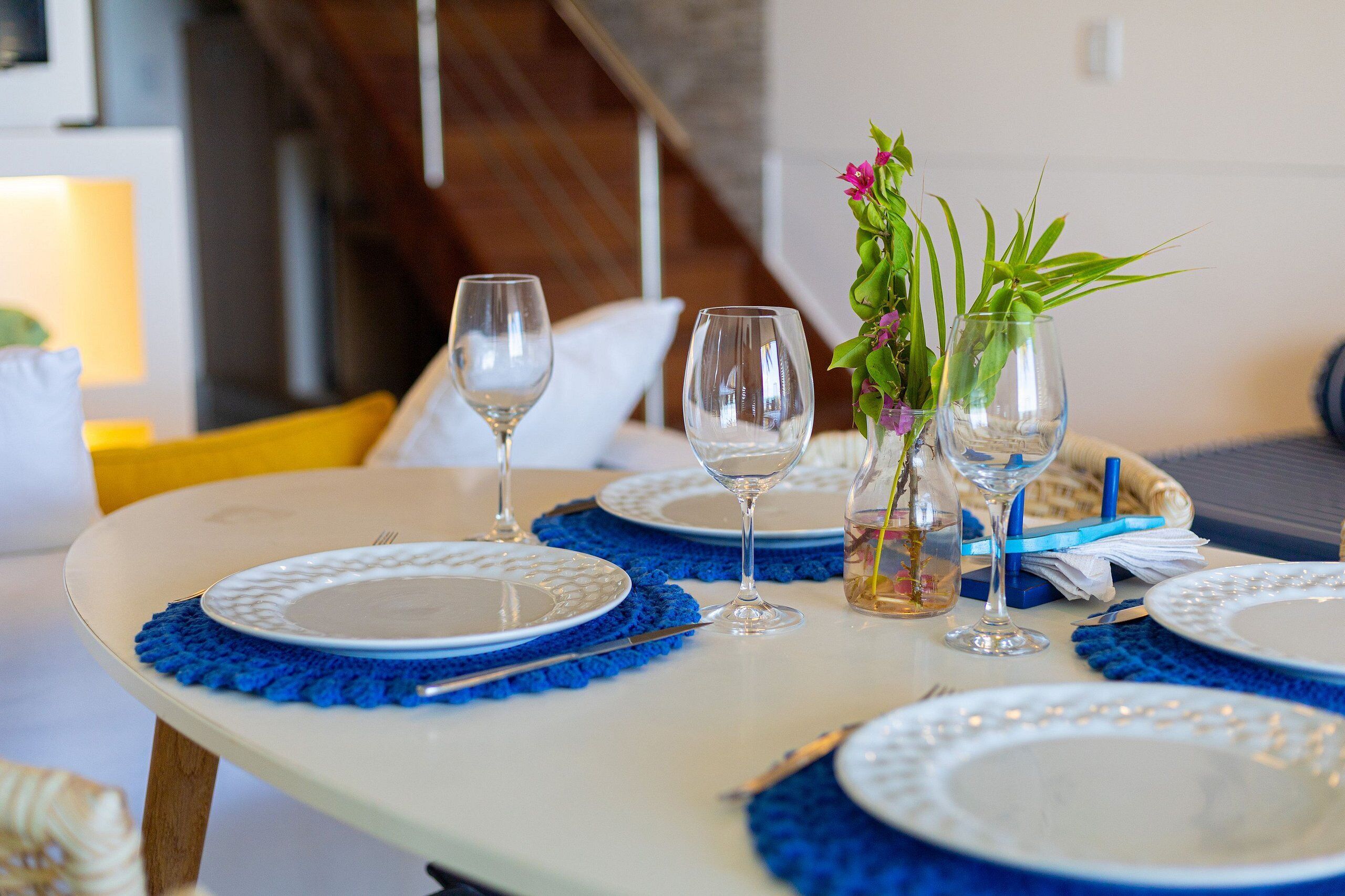 Une table à manger dressée avec des sets de table bleus, des assiettes blanches et des verres transparents.