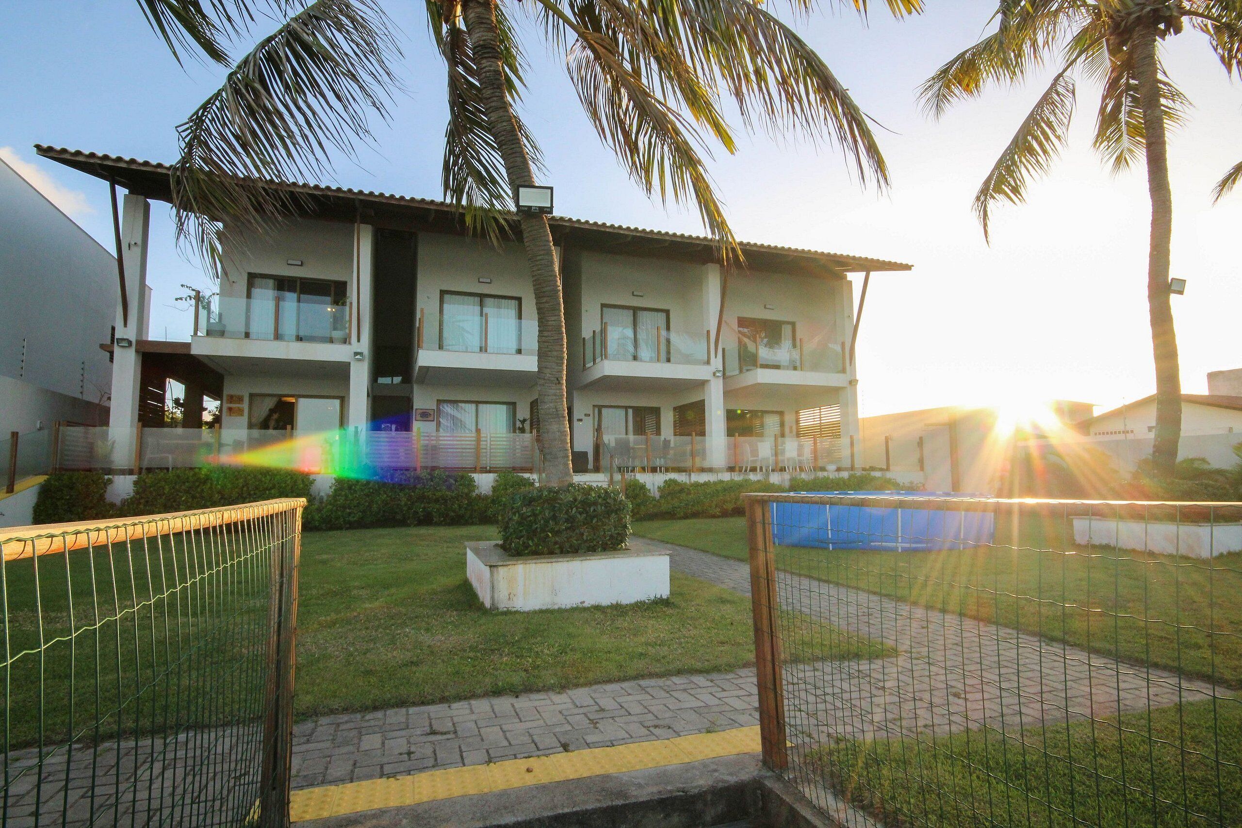 A multi-story hotel with balconies, a grassy lawn, and palm trees.