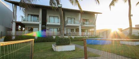 A multi-story hotel with balconies, a grassy lawn, and palm trees.