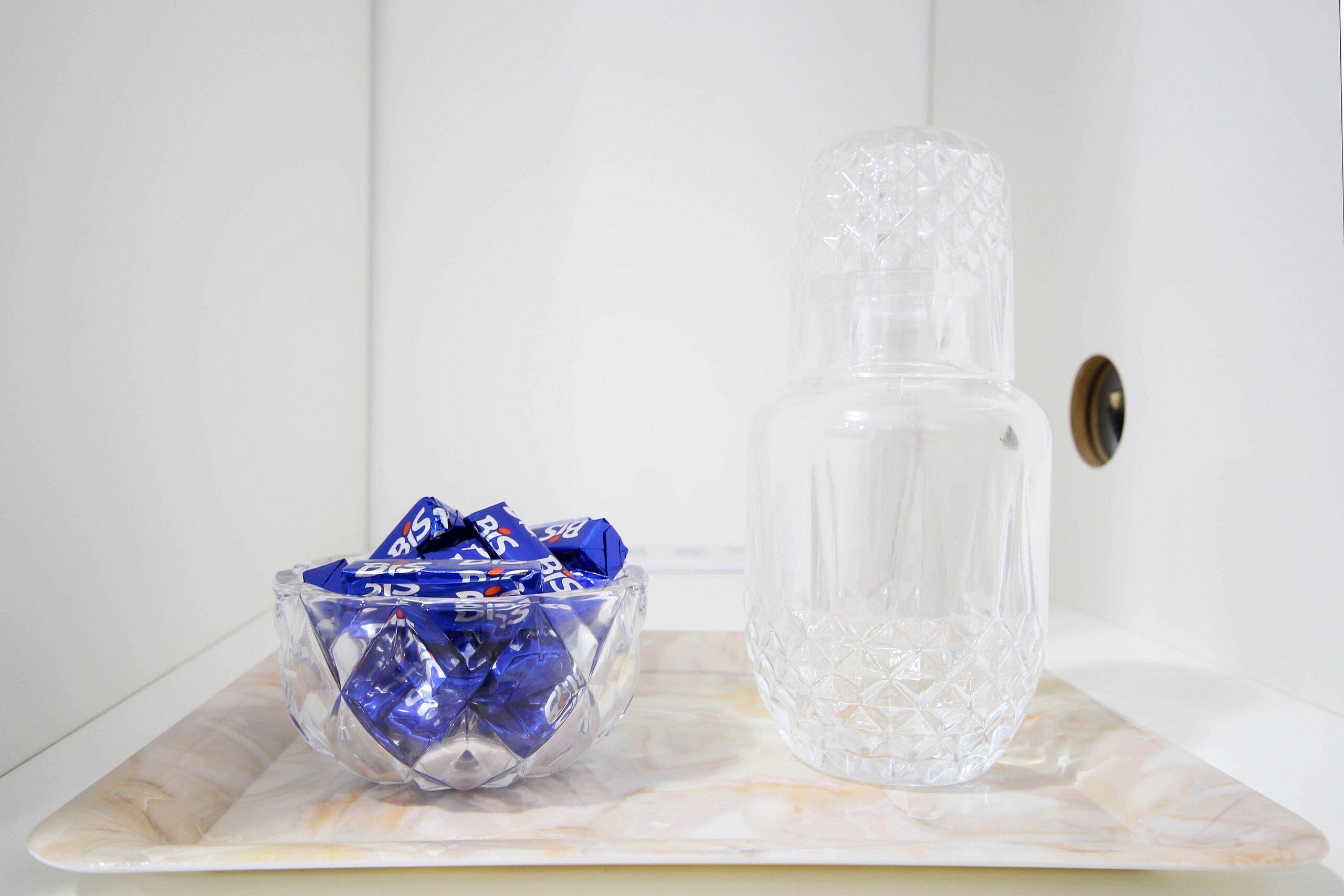 A clear glass bottle and a bowl filled with blue packets on a marble tray.