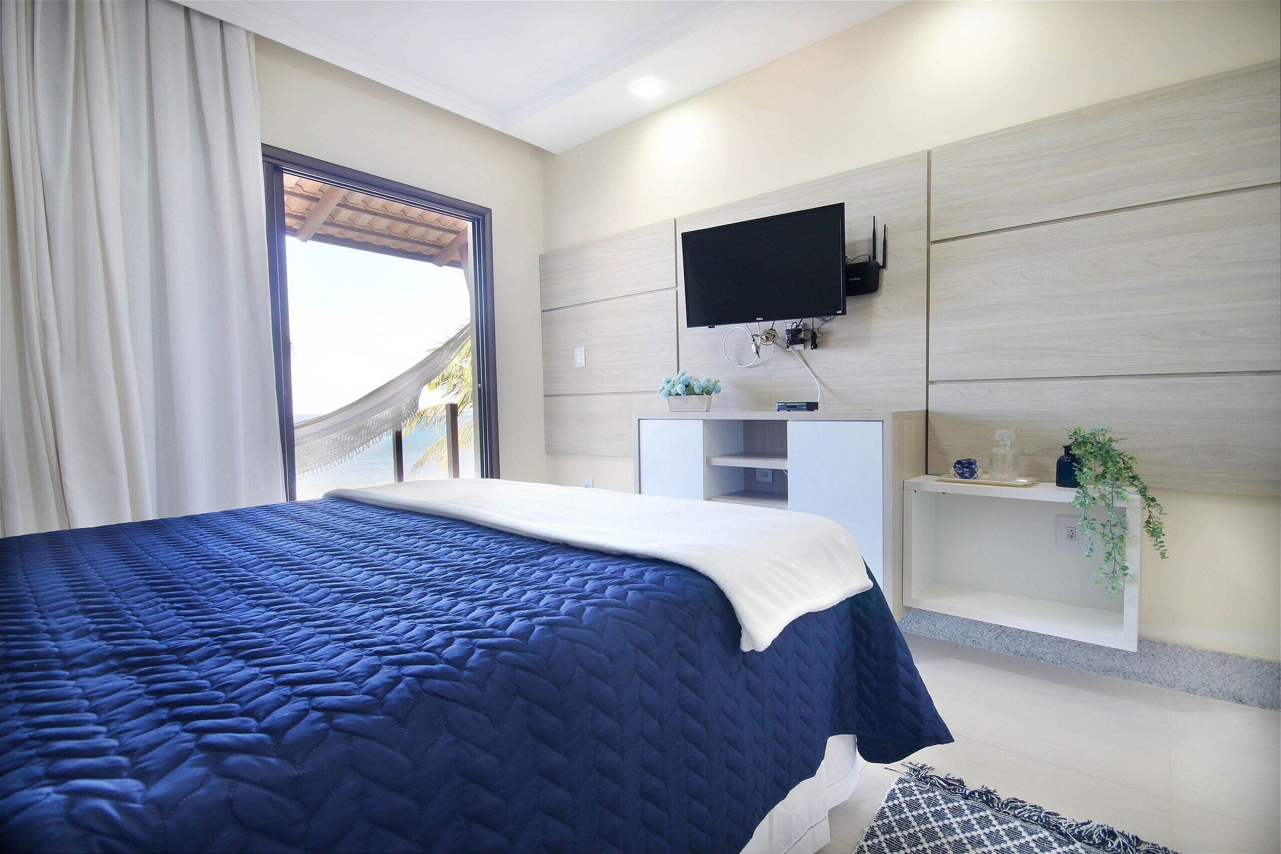 Een slaapkamer met een groot bed, een tv aan de muur en een raam met gordijnen.