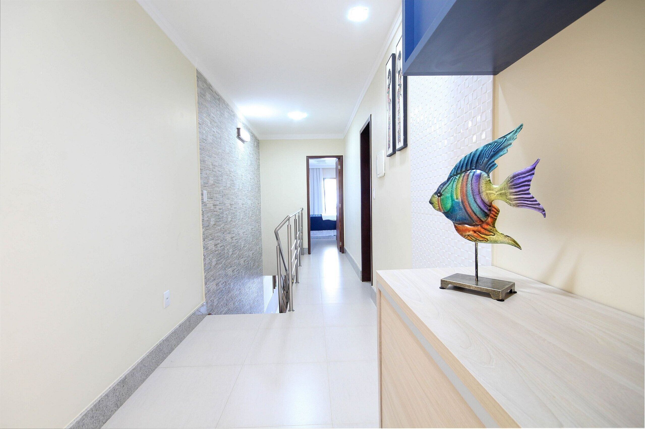 Un pasillo con piso de baldosas, barandilla de metal y una escultura decorativa de pez sobre un pedestal.