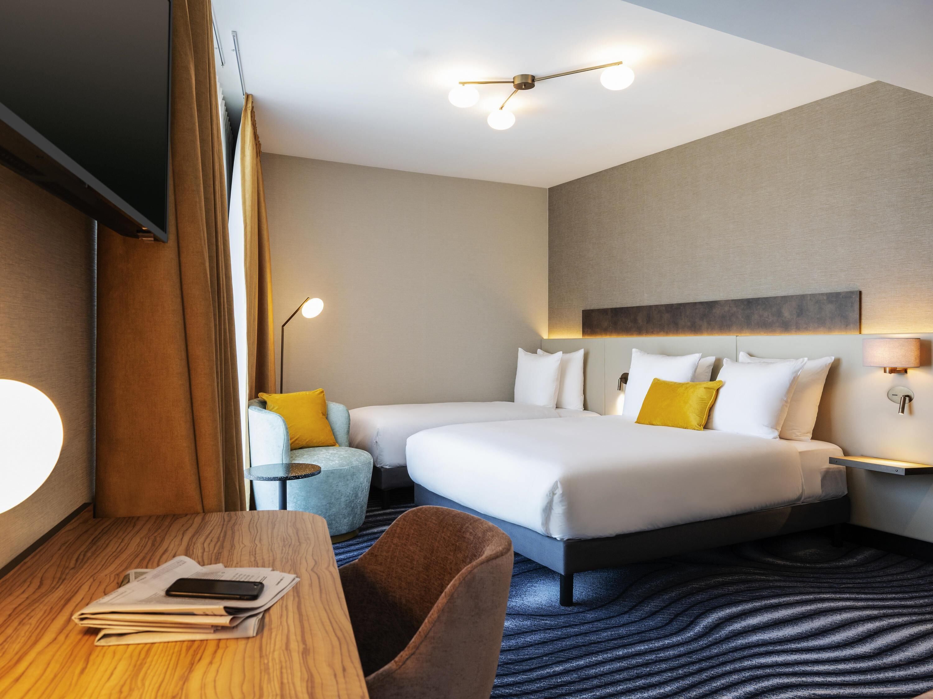 Habitación de hotel con dos camas, un escritorio con una silla, una lámpara y una lámpara de techo.
