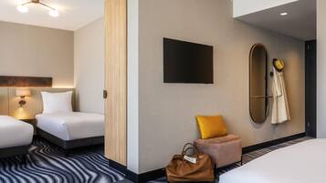 A hotel room with two beds, a large mirror, a flat-screen TV, a handbag, and a small ottoman.