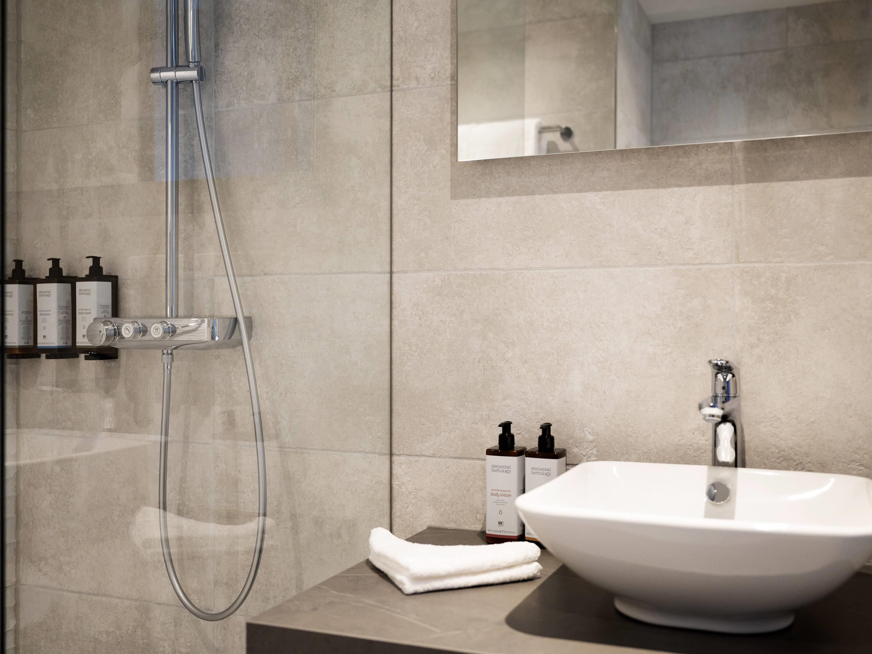 A modern bathroom with a shower, a sink, and toiletries on the counter.