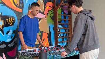Due persone giocano a calcio balilla in una stanza con un muro decorato con graffiti colorati.