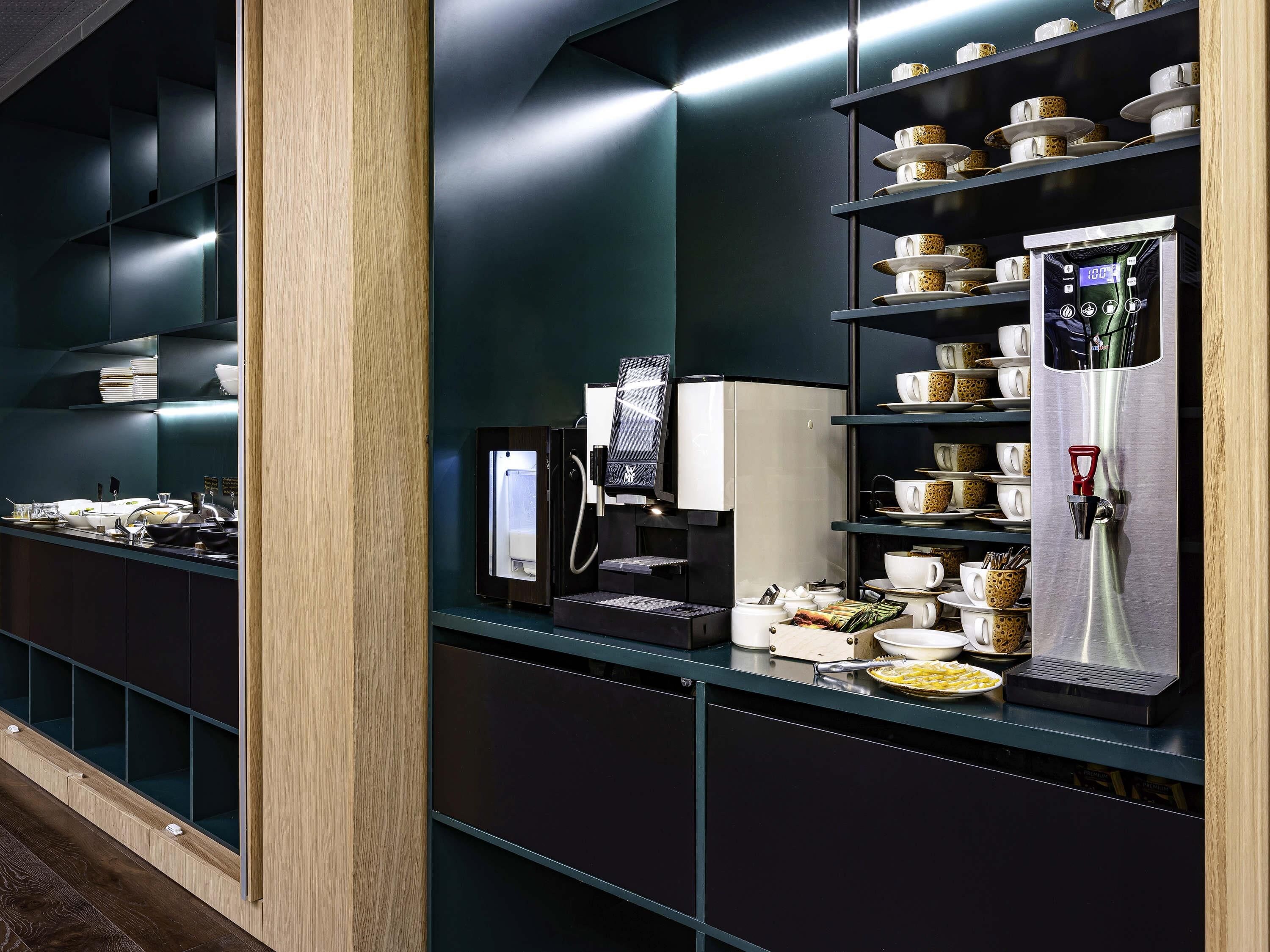 A modern kitchen with a coffee machine, shelves with cups, and a counter with food items.