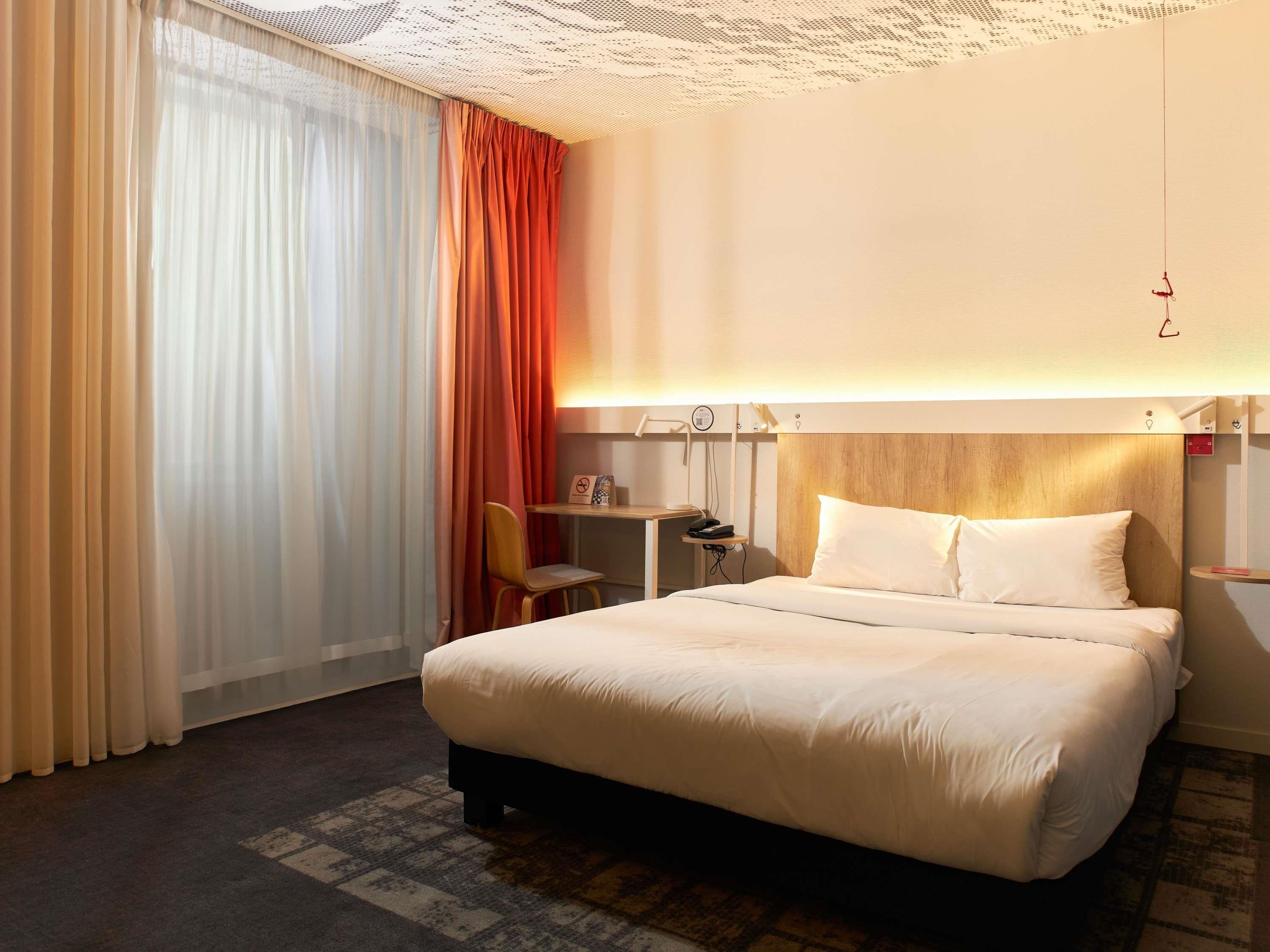 A hotel room with a bed, a desk, a chair, and a large window with curtains.