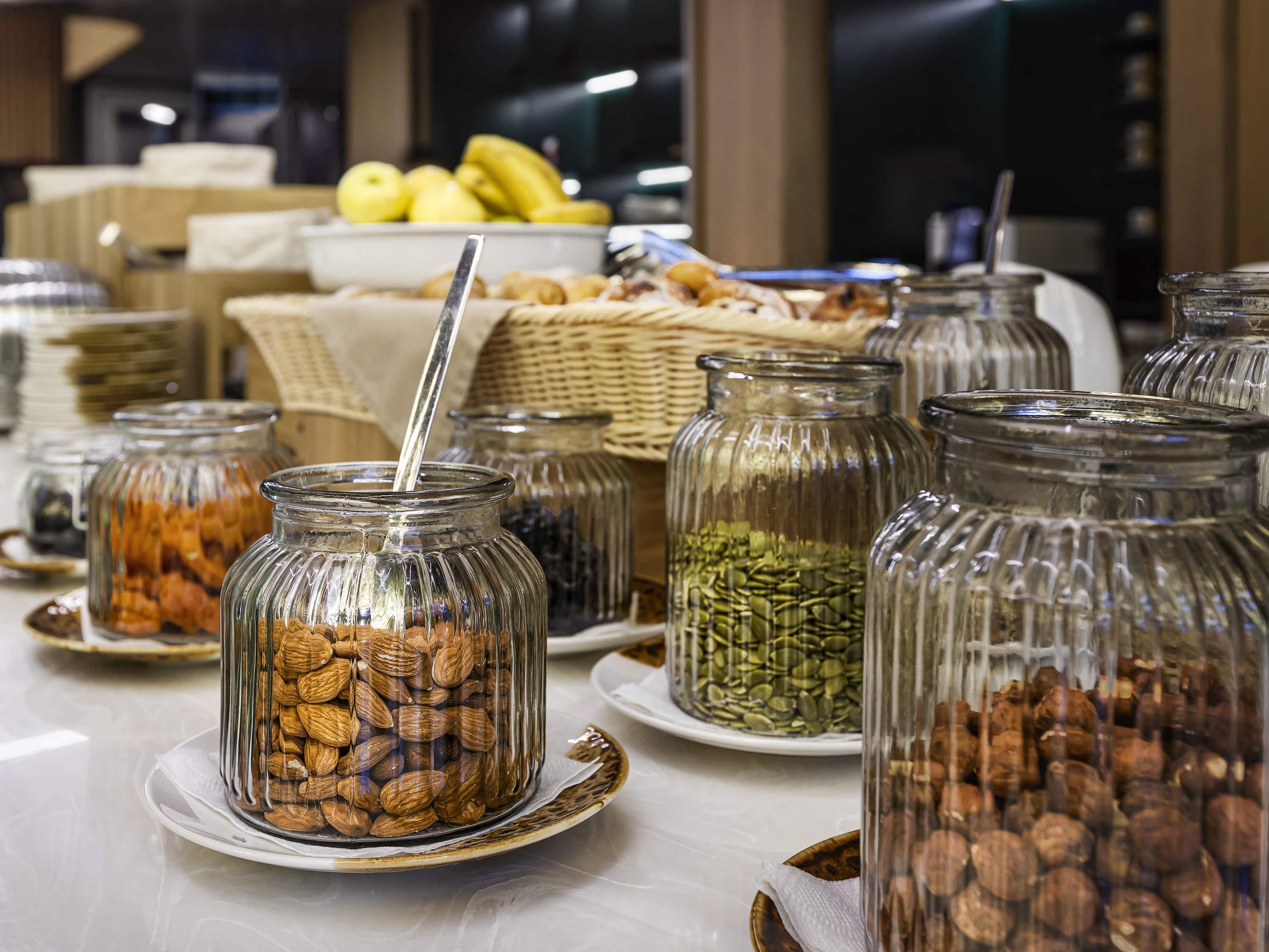 A buffet with various food items in glass jars, including nuts and seeds, and a basket of bananas in the background.