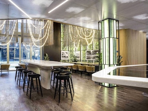 A modern bar area with a curved counter, black bar stools, and a ceiling with a perforated pattern. - Ibis Almaty Jetisu (Almaty)
