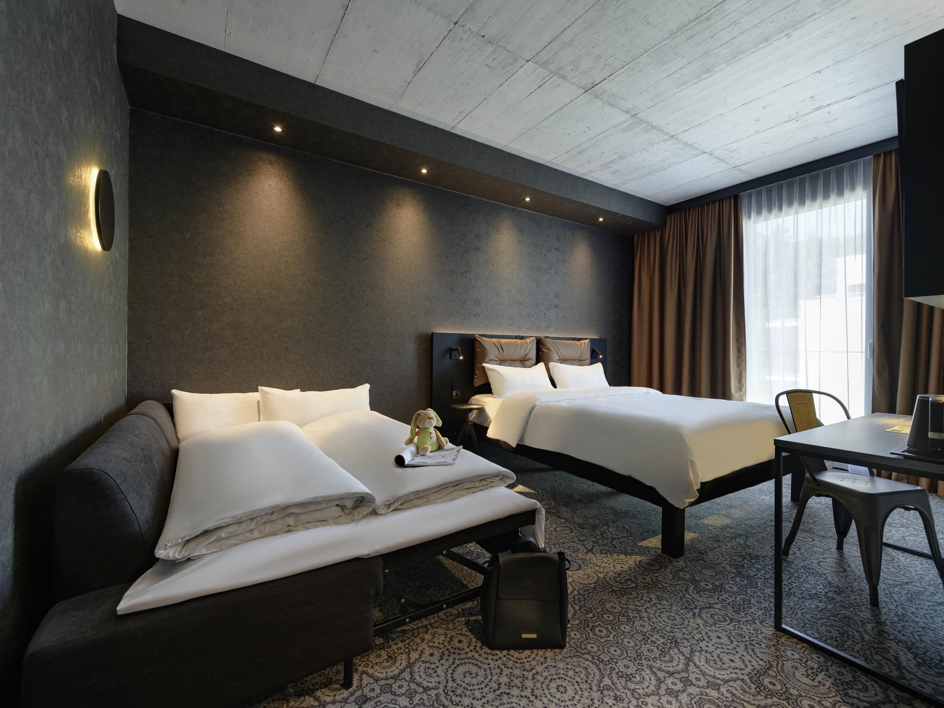 A hotel room with two beds, a sofa, a desk, and a chair.