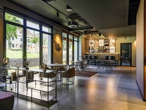 Un intérieur moderne avec de grandes fenêtres, un espace salon avec des tables et des chaises, et un mur orné d’œuvres d’art encadrées.