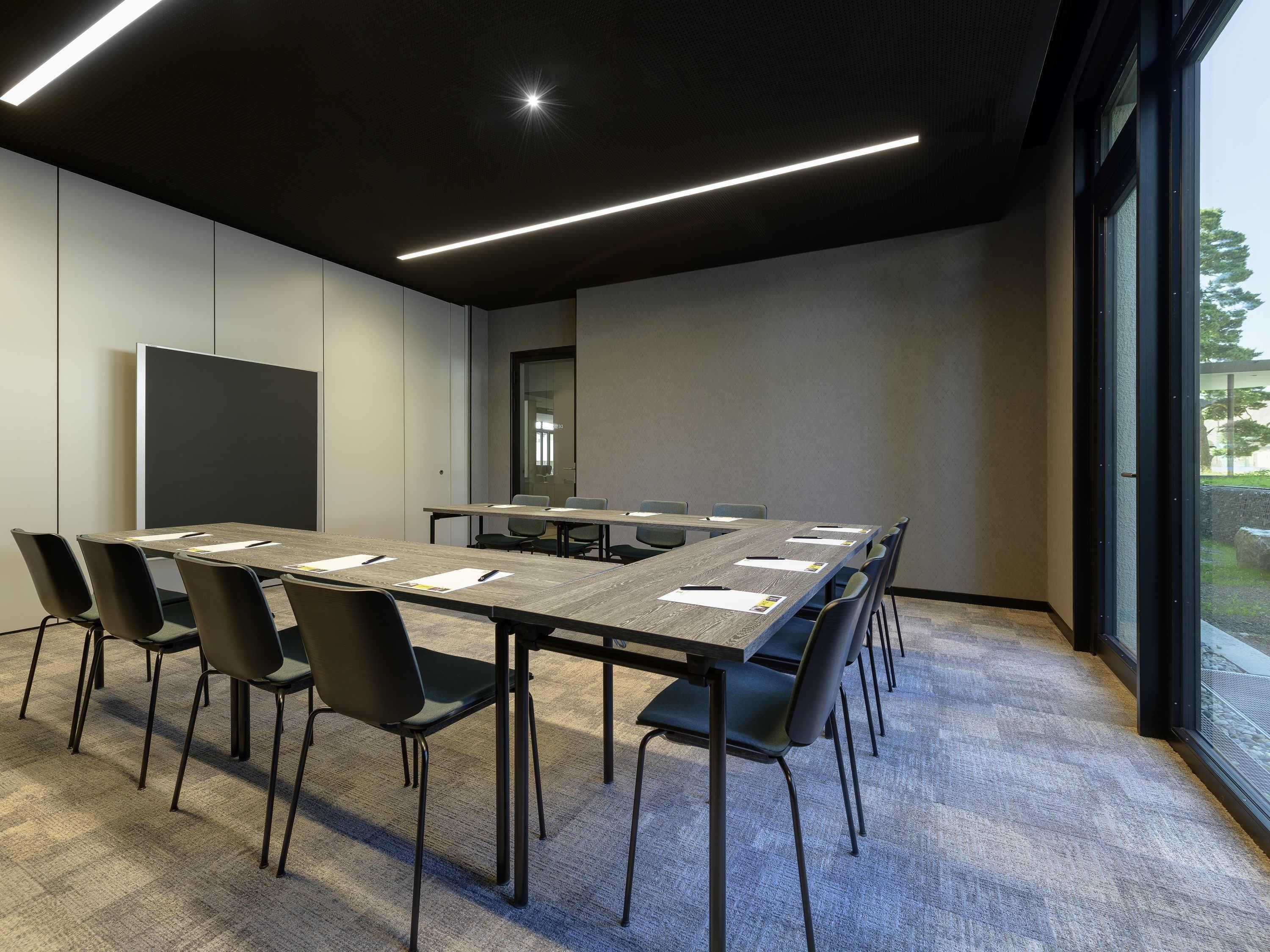 Une salle de conférence avec une longue table, des chaises, un écran de projection et une grande fenêtre.