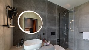 Een moderne badkamer met een grote ovaalwastafel, een ronde spiegel, een douche met glazen wand en een toilet.